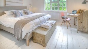 A bedroom with a large bed, a desk with a laptop, a chair, and a window with a view of greenery. - The Coach House (Pwllheli)