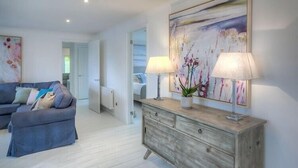 A modern living room with a sofa, a wooden sideboard, and a painting. - The Coach House (Pwllheli)