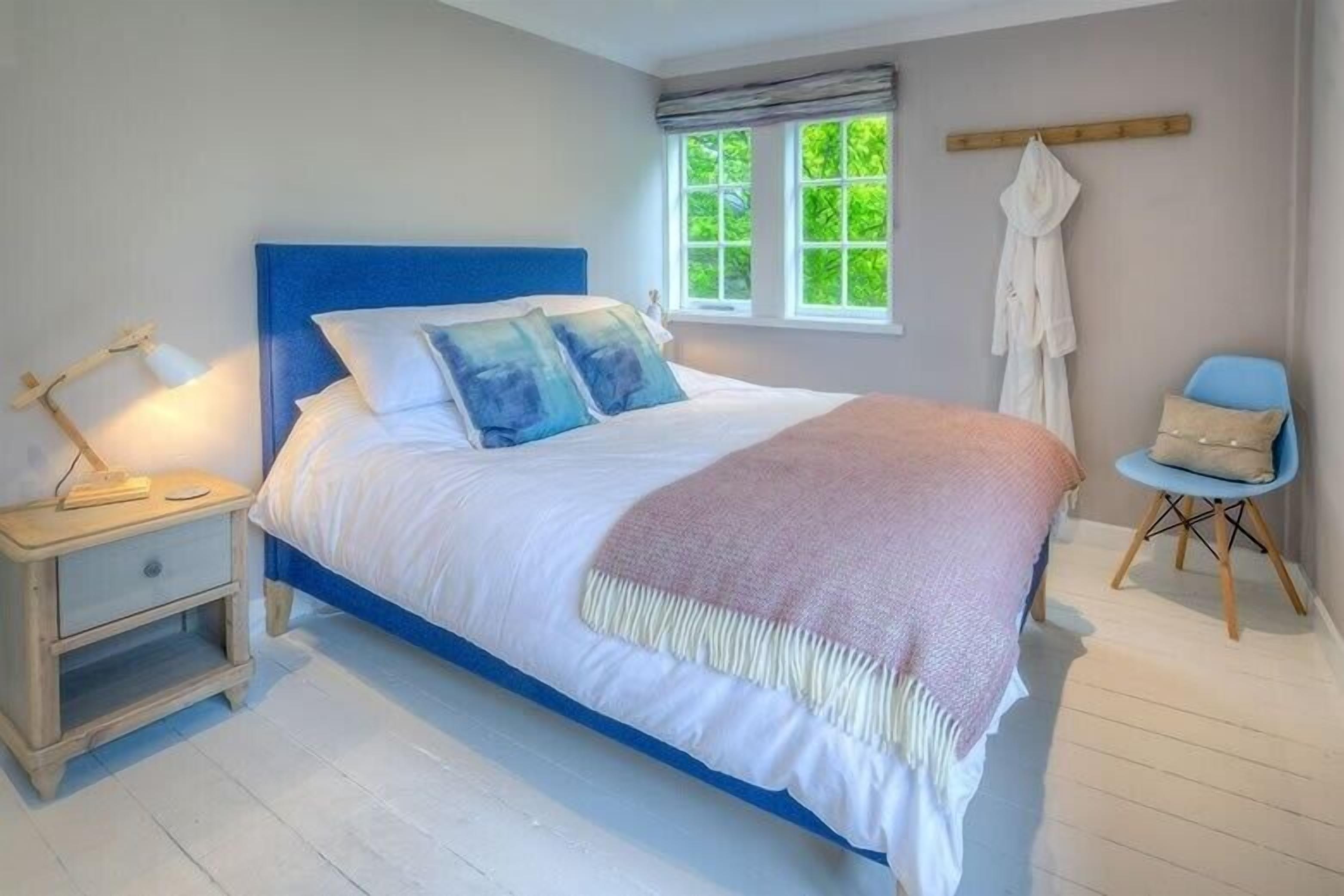 A bedroom with a bed, bedside table, chair, window, and a robe hanging on the wall.