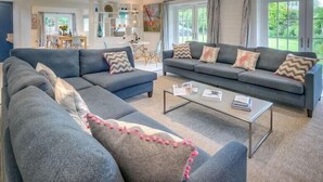 A modern living room with two grey sofas, a coffee table, and a dining area in the background. - The Coach House (Pwllheli)