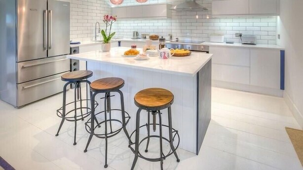 A modern kitchen with a central island, stainless steel appliances, and bar stools. - The Coach House (Pwllheli)