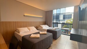 A modern hotel room with two beds, a large window with a view of buildings, and a flat-screen TV. - Pousada Duas Ilhas (Penha)