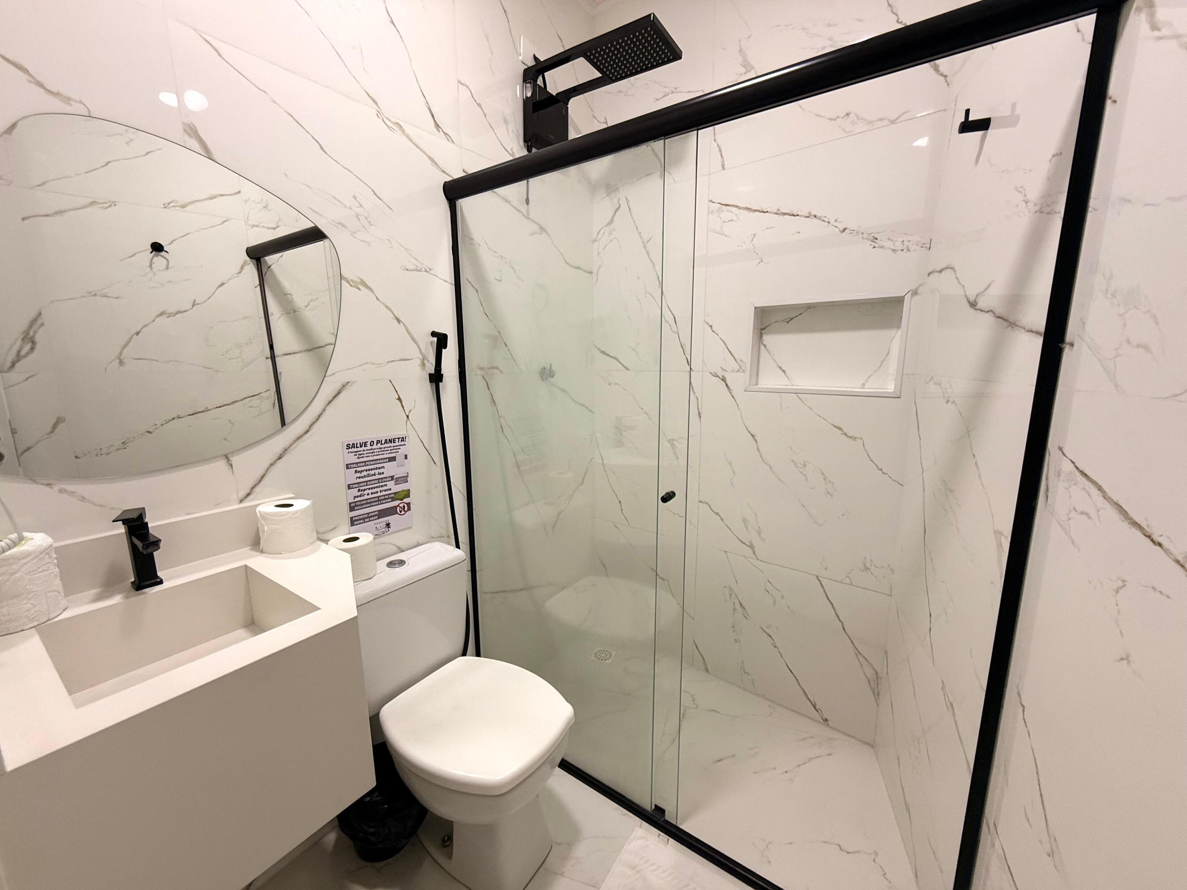 A modern bathroom with a glass-enclosed shower, a white toilet, and a sink with a mirror above it.