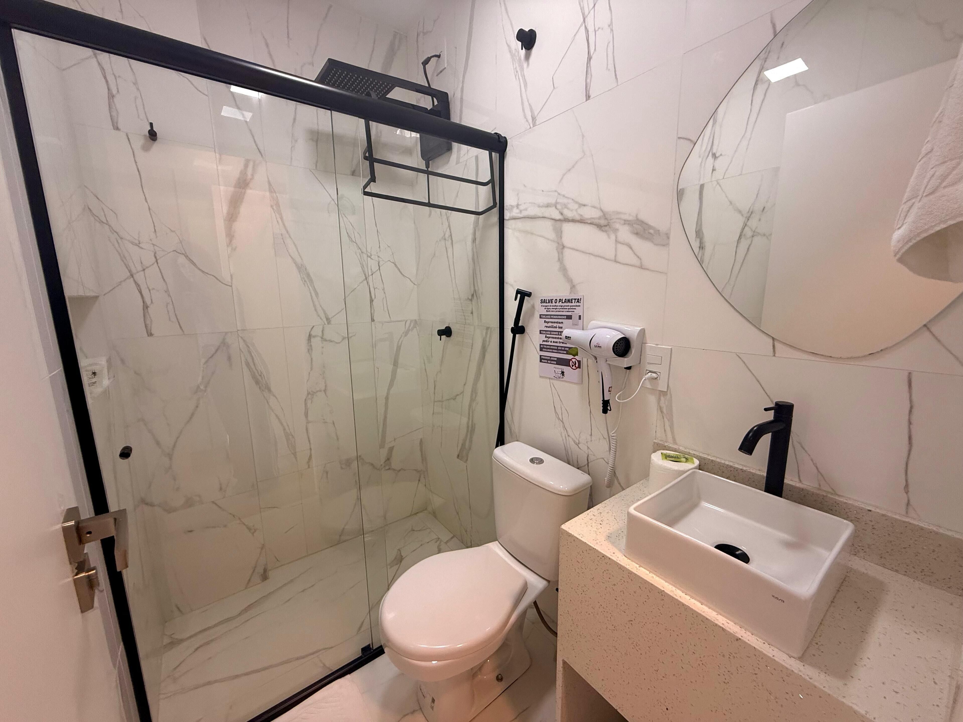 A bathroom with a glass shower enclosure, a toilet, a sink, and a mirror.
