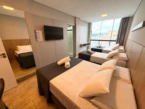 Camera d'albergo con tre letti, una TV a schermo piatto e un'ampia finestra con vista sulla città.