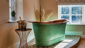 A bathroom with a green bathtub, a small round table with a metal base, and a potted plant. - A luxury barn conversion close to Grizedale Forest & Hawkshead village (Satterthwaite (Nr. Hawkshead))
