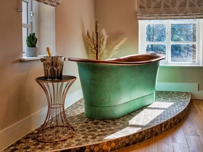 A bathroom with a green bathtub, a small round table with a metal base, and a potted plant.