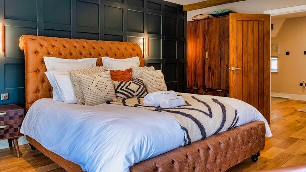 A bedroom with a large bed, dark wall paneling, a wooden wardrobe, and a wooden ceiling beam. - A luxury barn conversion close to Grizedale Forest & Hawkshead village (Satterthwaite (Nr. Hawkshead))