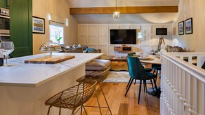 A modern kitchen with a central island, wooden beams, a chandelier, and a large flat-screen TV. - A luxury barn conversion close to Grizedale Forest & Hawkshead village (Satterthwaite (Nr. Hawkshead))