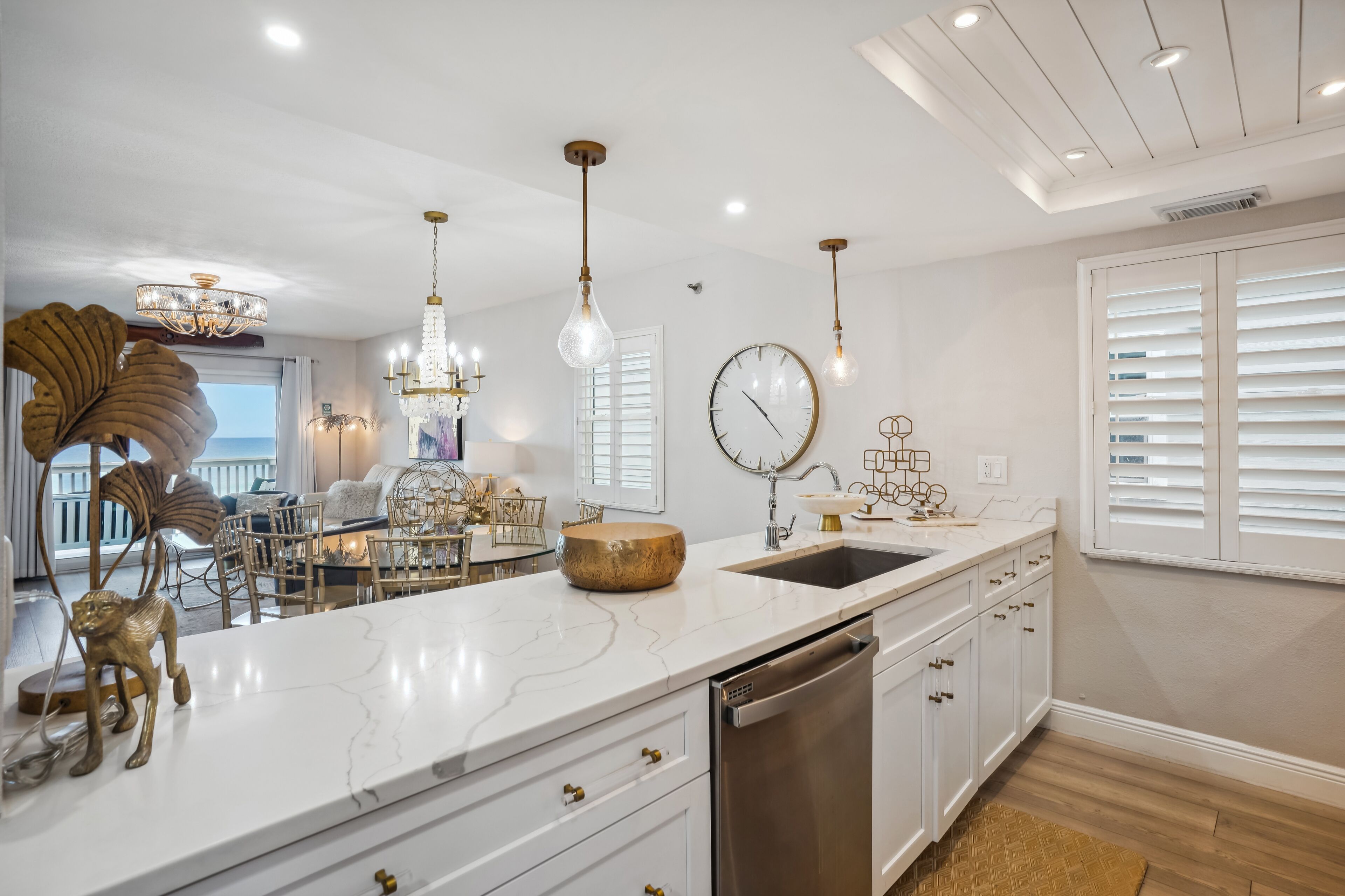 A modern kitchen with a marble countertop, stainless steel dishwasher, and pendant lighting.