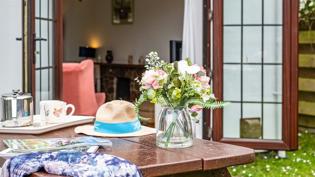 A wooden table with a hat, a vase with flowers, a tray with a teapot and cups, and a magazine. - Hazelhurst (Wadebridge)