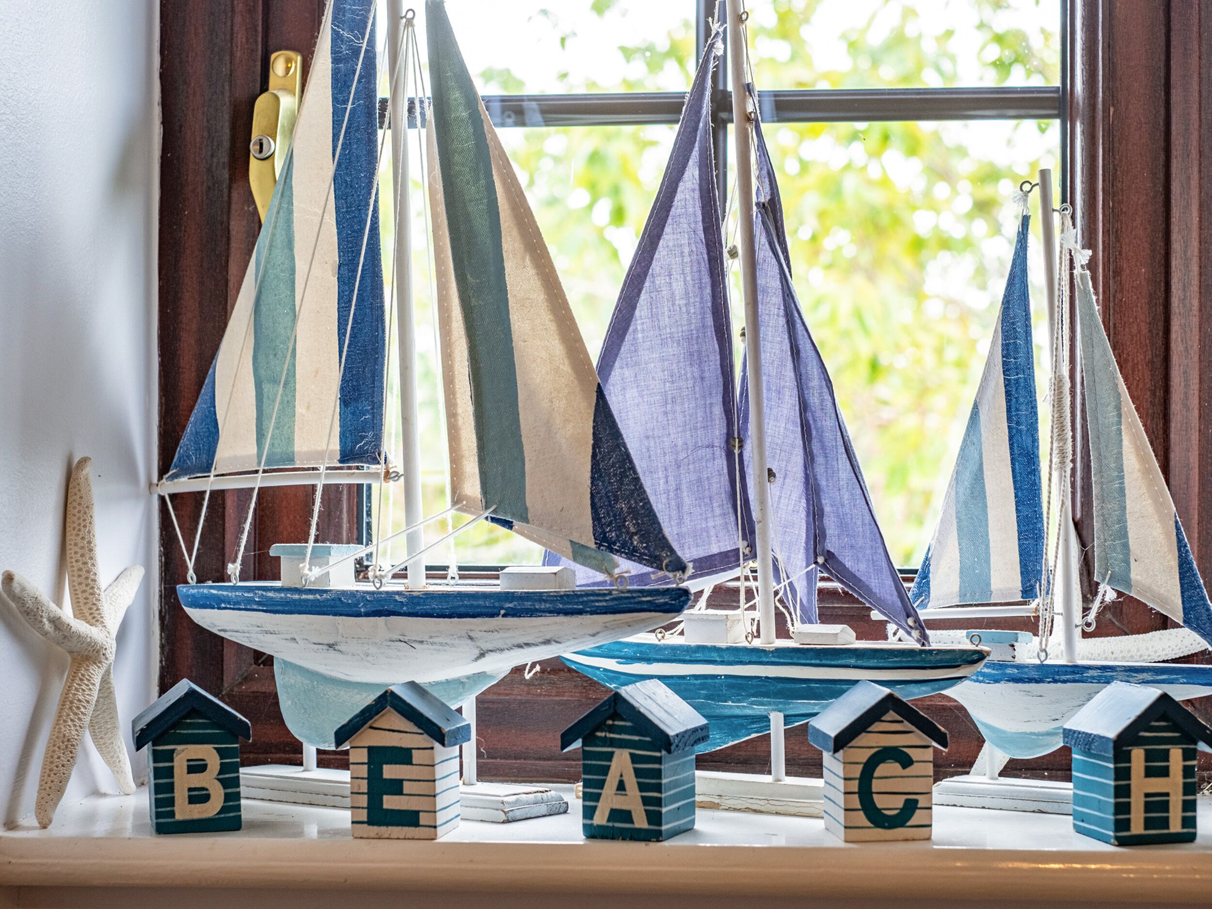 A model sailboat collection on a windowsill with alphabet blocks labeled B, E, A, C, and H.