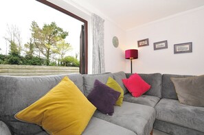 A grey sofa with colorful cushions, a red floor lamp, and framed pictures on the wall. - Hazelhurst (Wadebridge)