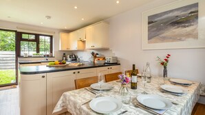 A modern kitchen with white cabinets, a black countertop, and a dining area set for four with a table set for a meal. - Hazelhurst (Wadebridge)