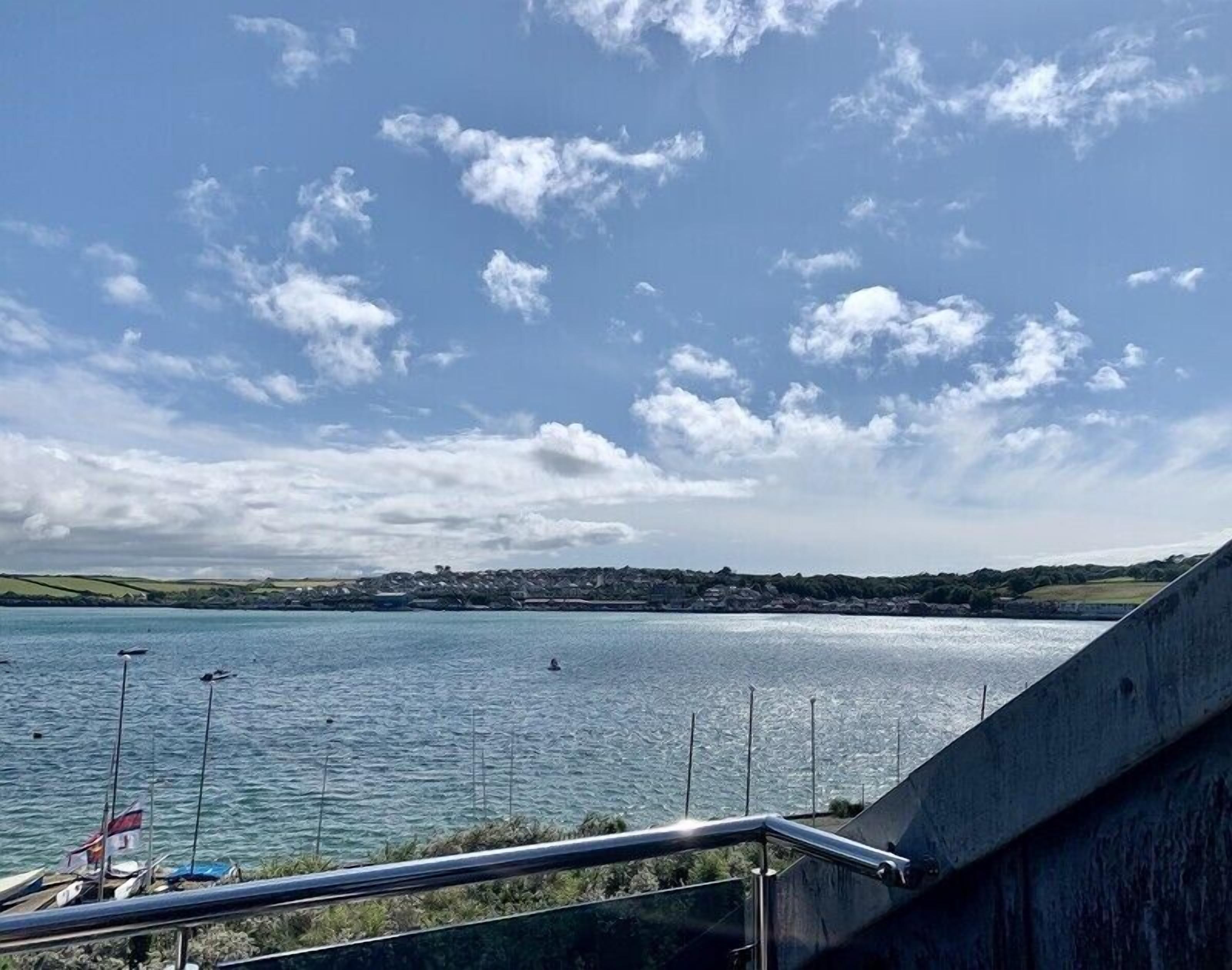 A coastal view with a clear sky, calm sea, and a distant shoreline with buildings.