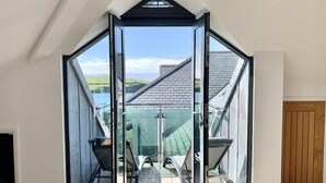 A room with a large glass door leading to an outdoor patio area with a table and chairs. - Upper Deck (Wadebridge)