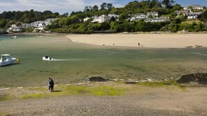 A coastal beach with clear waters, a sandy shore, and houses in the background. - Upper Deck (Wadebridge)