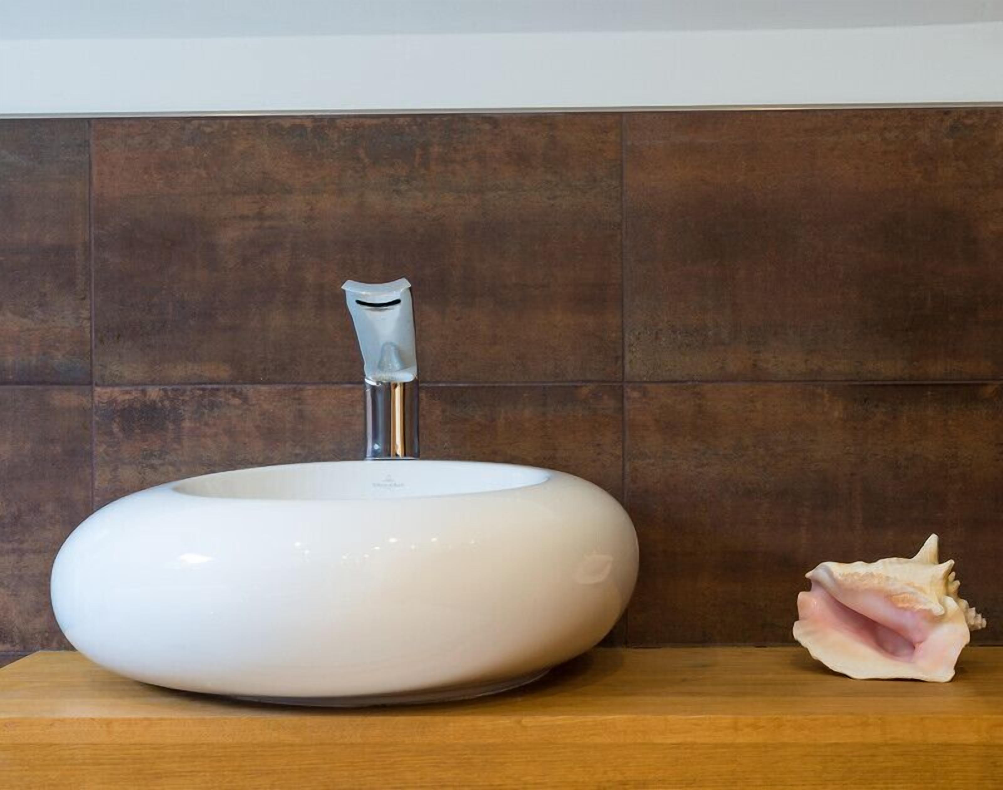 A white oval sink with a modern faucet against a tiled wall.