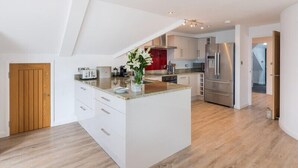 A modern kitchen with white cabinetry, a central island, and a stainless steel refrigerator. - Upper Deck (Wadebridge)