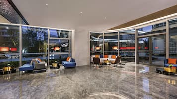 A modern lounge area with seating and a glass wall offering a city view.