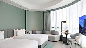 Et moderne hotelværelse med to senge, en sofa, et fjernsyn og et lille bord.