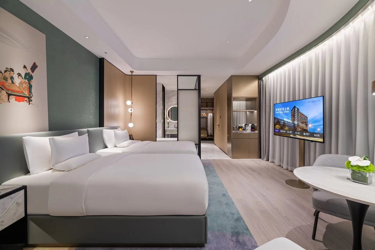 Quarto de hotel moderno com uma cama grande, uma mesa e uma televisão.
