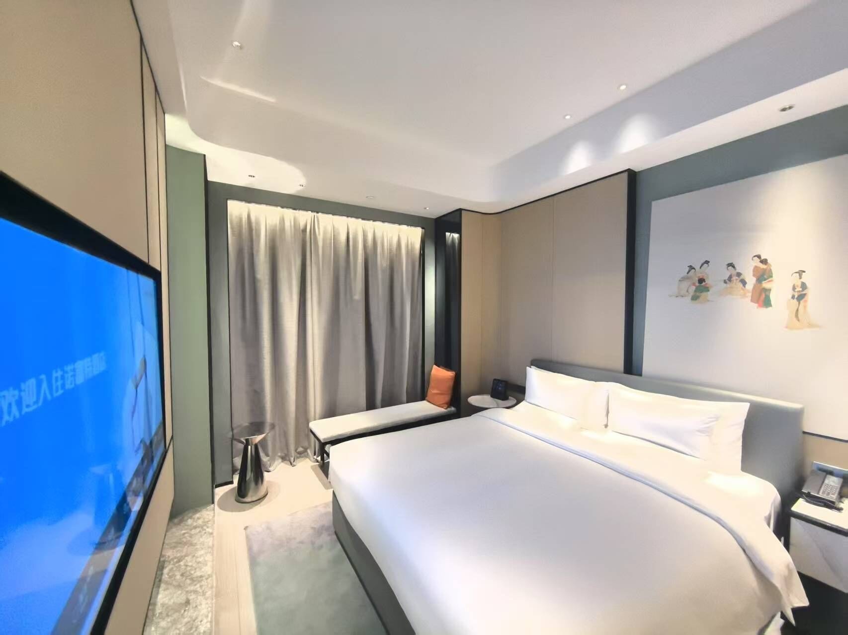 Habitación de hotel moderna con una cama grande, televisor de pantalla plana, mesita de noche y una pared decorada con obras de arte.