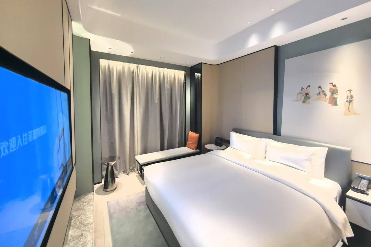 Quarto de hotel moderno com uma cama grande, televisão de tela plana, mesa de cabeceira e uma parede com obras de arte.