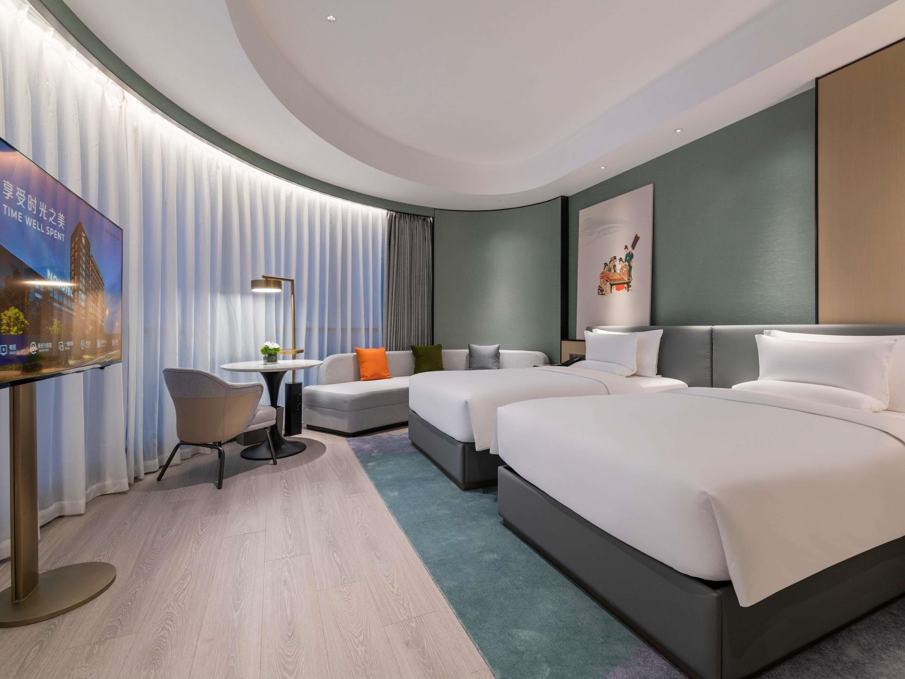 A hotel room with a large bed, a sofa, a small table, and a TV.