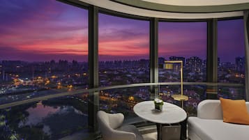 A modern room with a curved glass wall, a round table with a plant, a sofa with a cushion, and a floor lamp.
