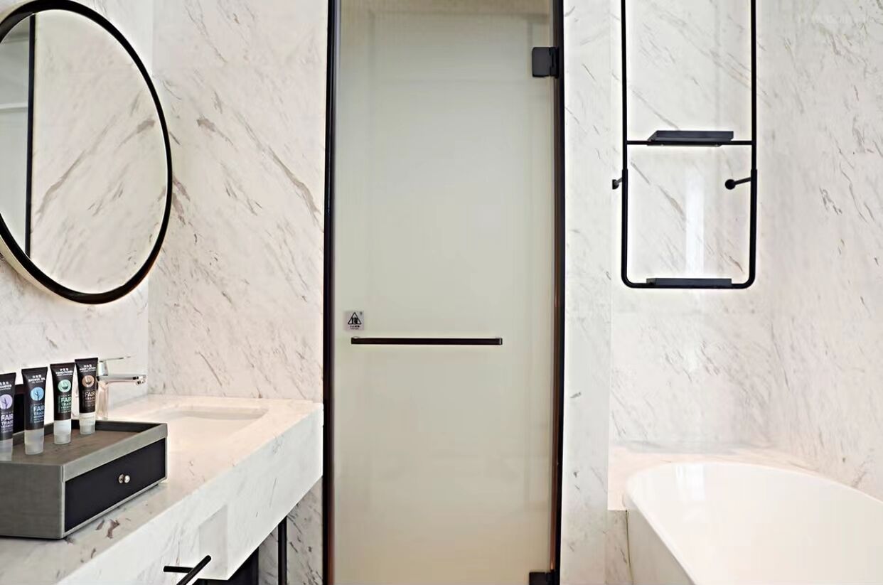 A modern bathroom with a marble countertop, a large mirror, a glass shower enclosure, and a white bathtub.