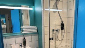 A modern bathroom with a glass-enclosed shower, a white sink, and a teal-colored wall. - Ibis Budget Nancy Laxou (Laxou)