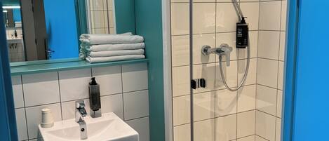 A modern bathroom with a glass-enclosed shower, a white sink, and a teal-colored wall.