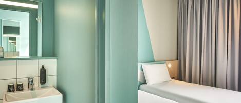 A modern hotel room with a white sink, a mirror, a bed with a white pillow, and a grey curtain.
