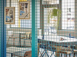 Una habitación con una mesa, sillas, un ventanal y un cartel en la pared.