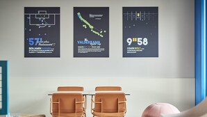A modern room with two brown chairs, a table, and a large poster on the wall. - Ibis Budget Nancy Laxou (Laxou)