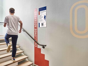 Una persona bajando una escalera con barandilla, un cartel en la pared y un código QR.