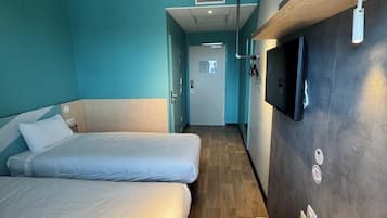 A hotel room with two beds, a wooden floor, a TV mounted on the wall, and a small table with a remote control.