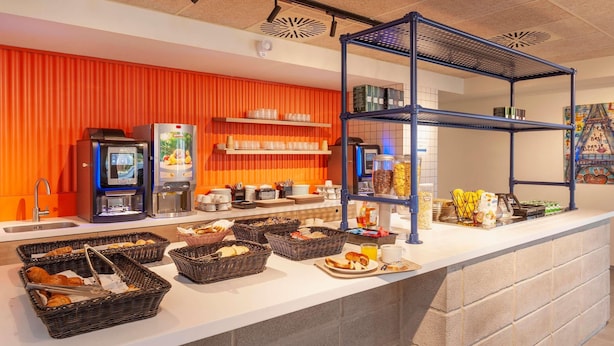 A breakfast buffet with various food items, coffee machines, and a blue shelving unit.