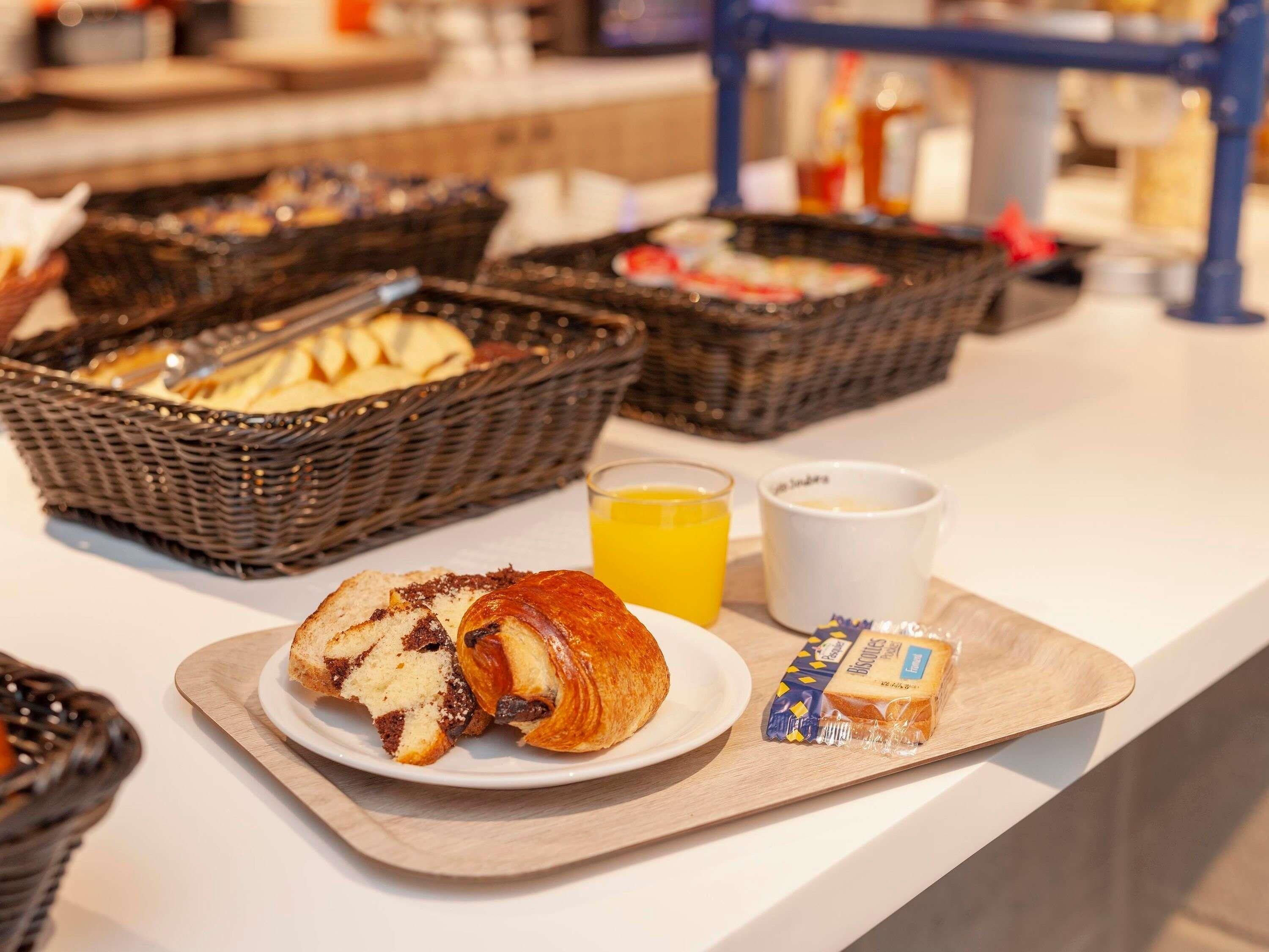 A breakfast buffet with bread, pastries, and juice.