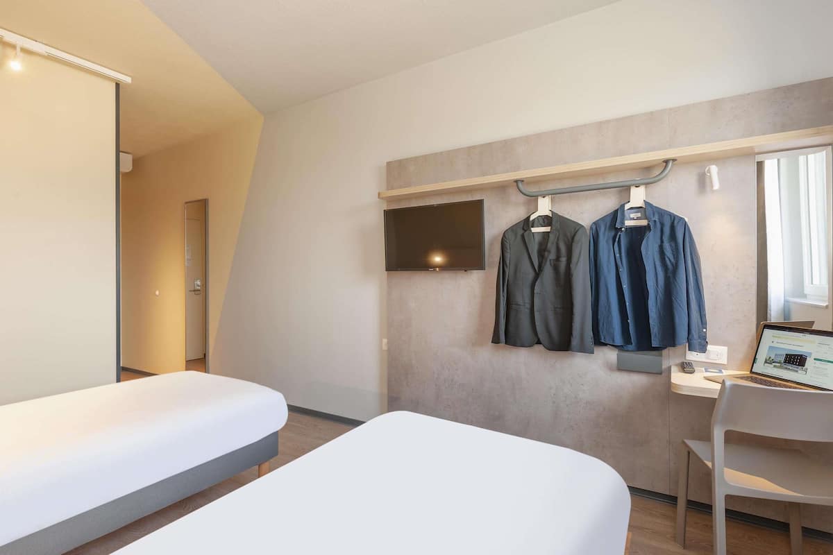 A hotel room with a bed, a desk, a chair, and a TV mounted on the wall.