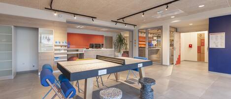 A modern indoor space with a ping pong table, seating, and a plant.