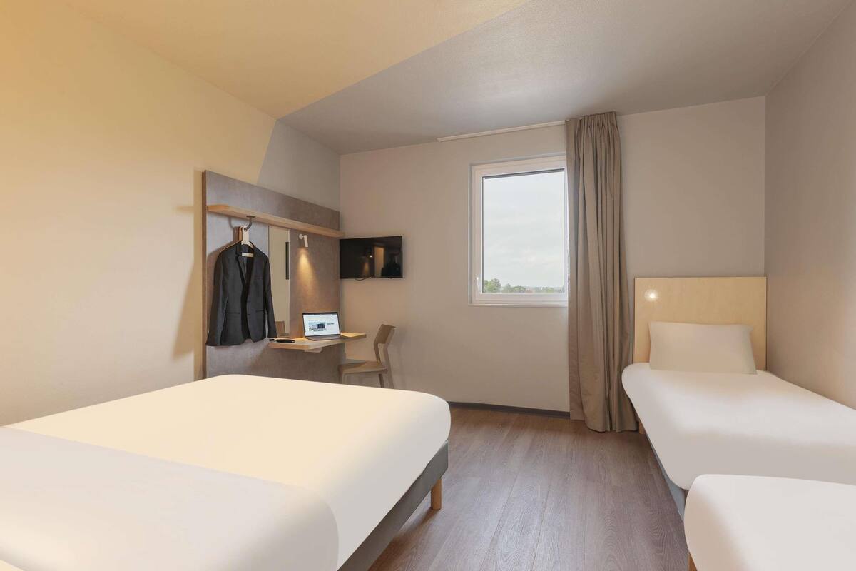 A hotel room with two beds, a desk with a laptop, a TV, and a window with curtains.