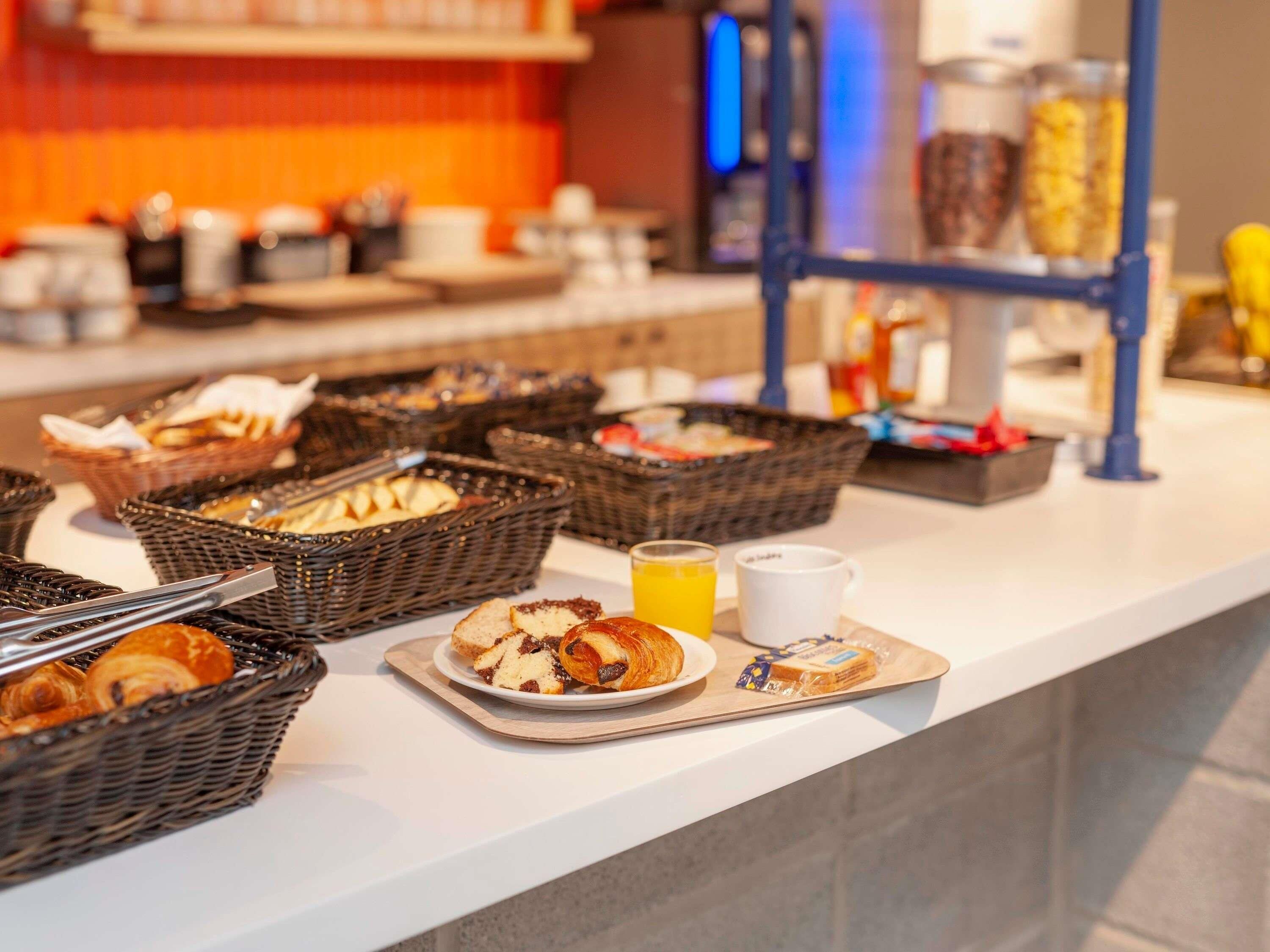 A breakfast buffet with baskets of pastries, a plate of croissants, a glass of orange juice, and a white mug.