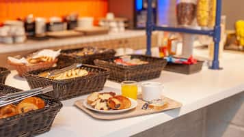 Ein Frühstücksbuffet mit Körben voller Gebäck, einer Croissantplatte, einem Glas Orangensaft und einer weißen Tasse.