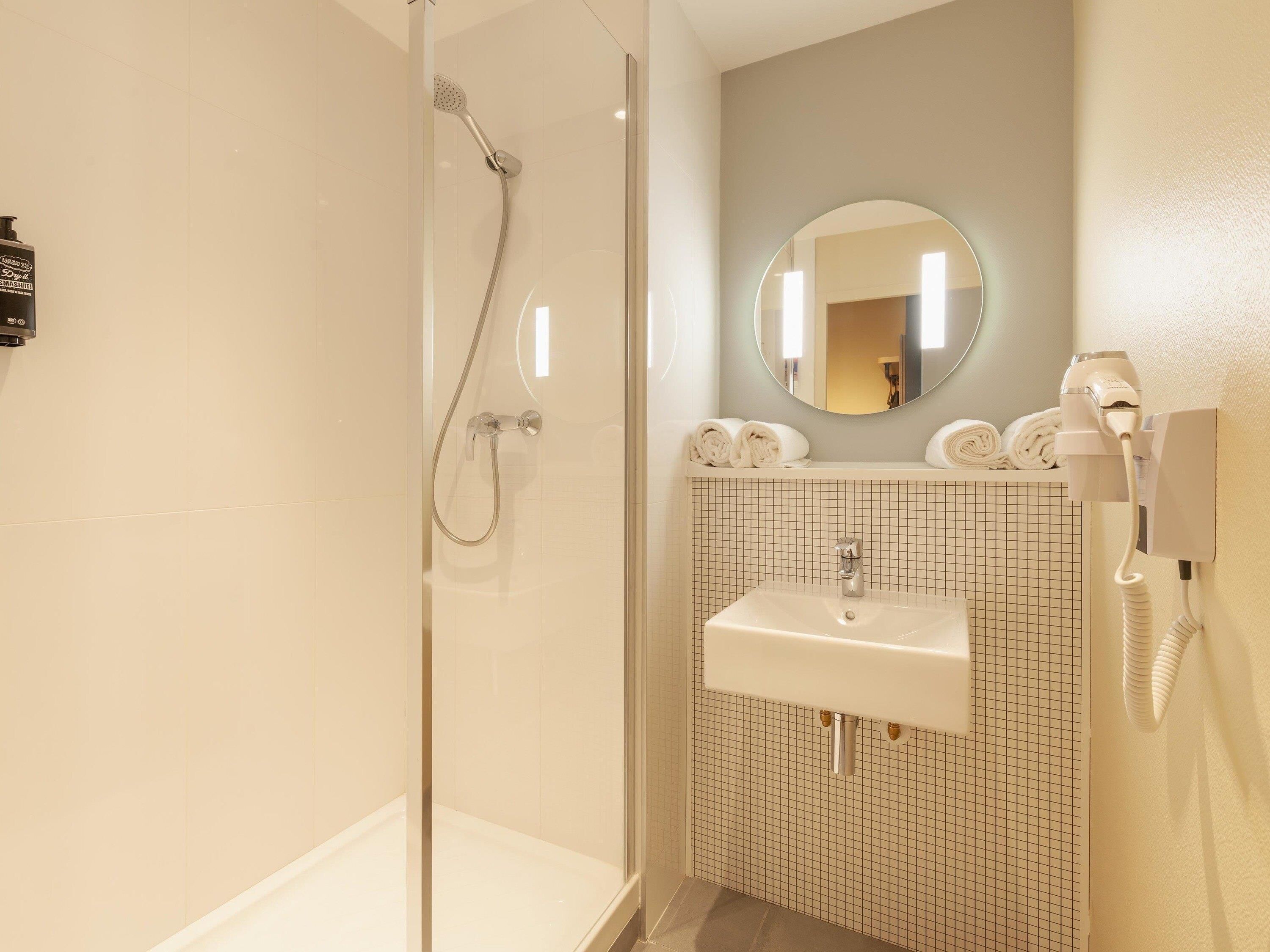 A bathroom with a glass-enclosed shower, a sink with a grid-patterned backsplash, and a hairdryer mounted on the wall.