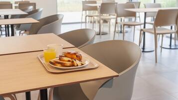Een moderne eetruimte met tafels en stoelen, een dienblad met toast en sinaasappelsap, en uitzicht op het groen.
