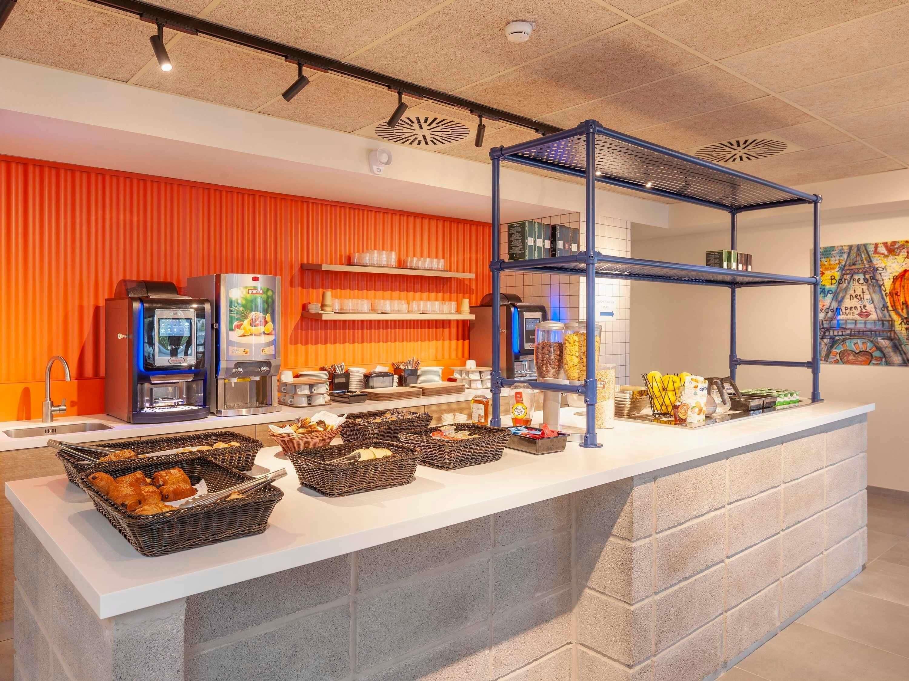 A breakfast bar with coffee machines, baskets of pastries, and shelves with condiments.