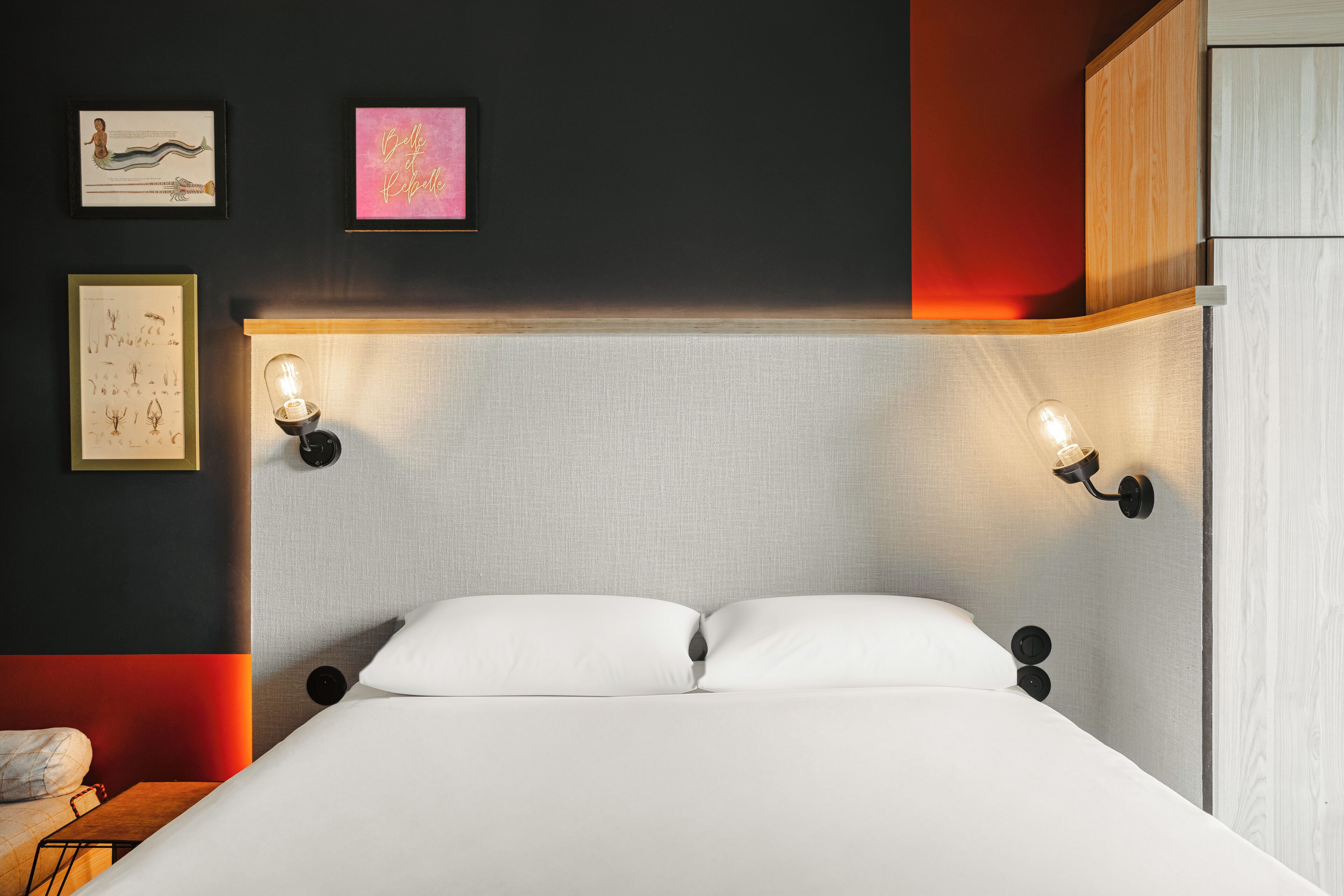 A modern bedroom with a large bed, two wall-mounted reading lights, and artwork on the wall.
