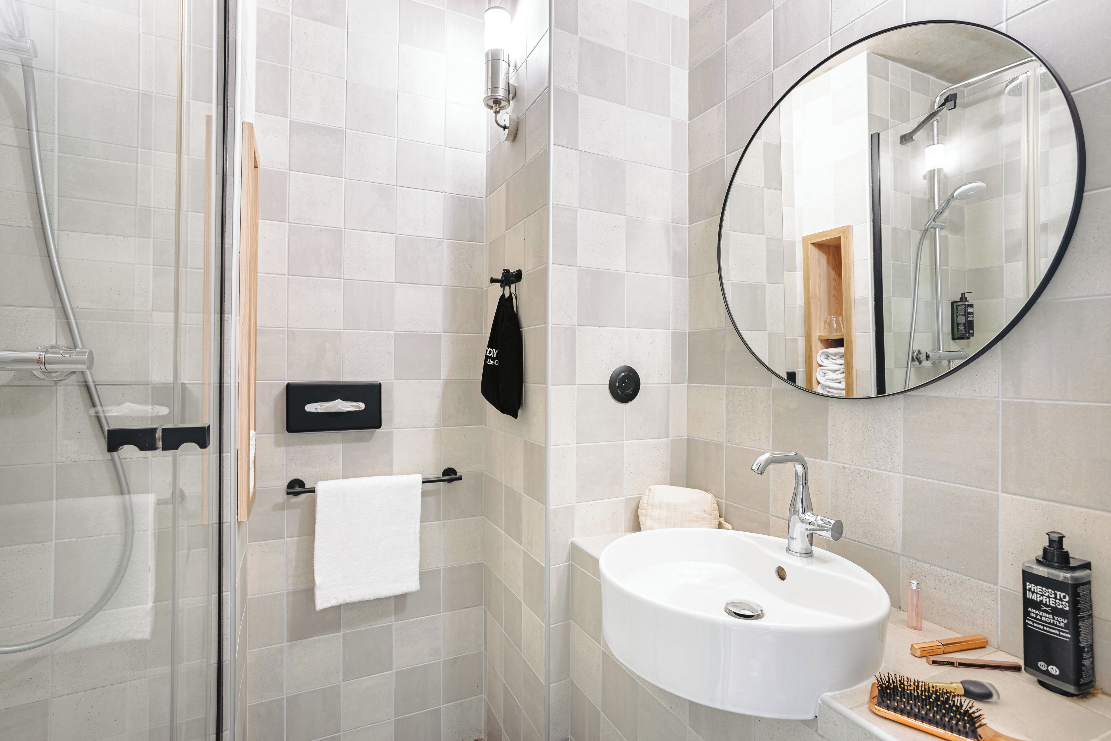 Un baño moderno con cabina de ducha de vidrio, un lavamanos blanco y un espejo redondo.